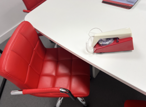 Picture of analogue red and white phone with SL-Complete branded mouse mats. In the foreground there is a red leather chair